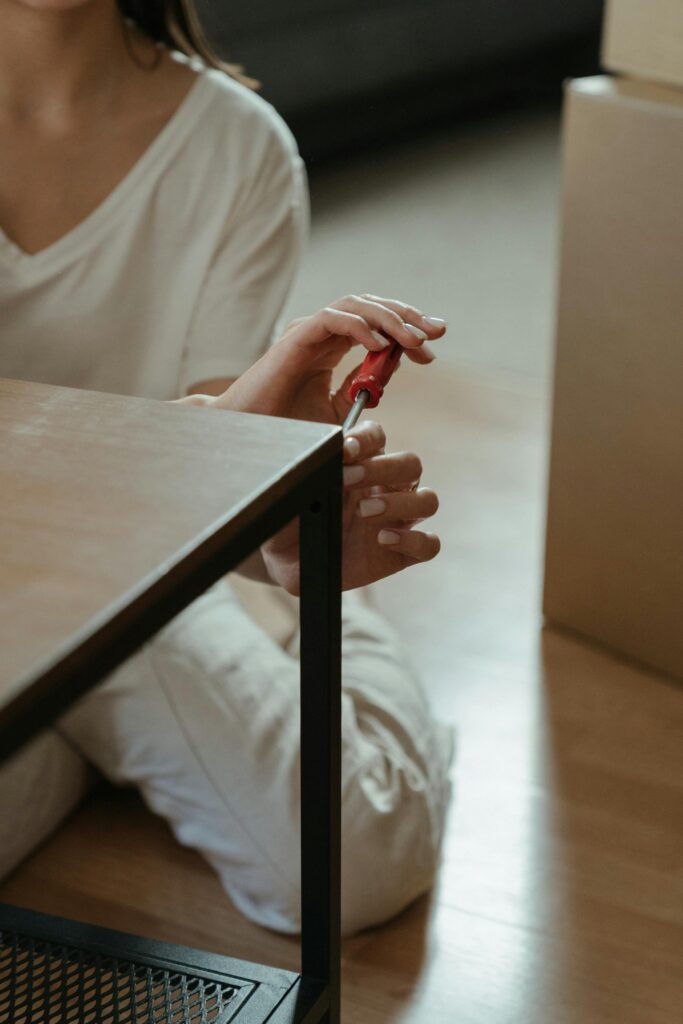 A woman using a screwdriver while assembling a table indoors.