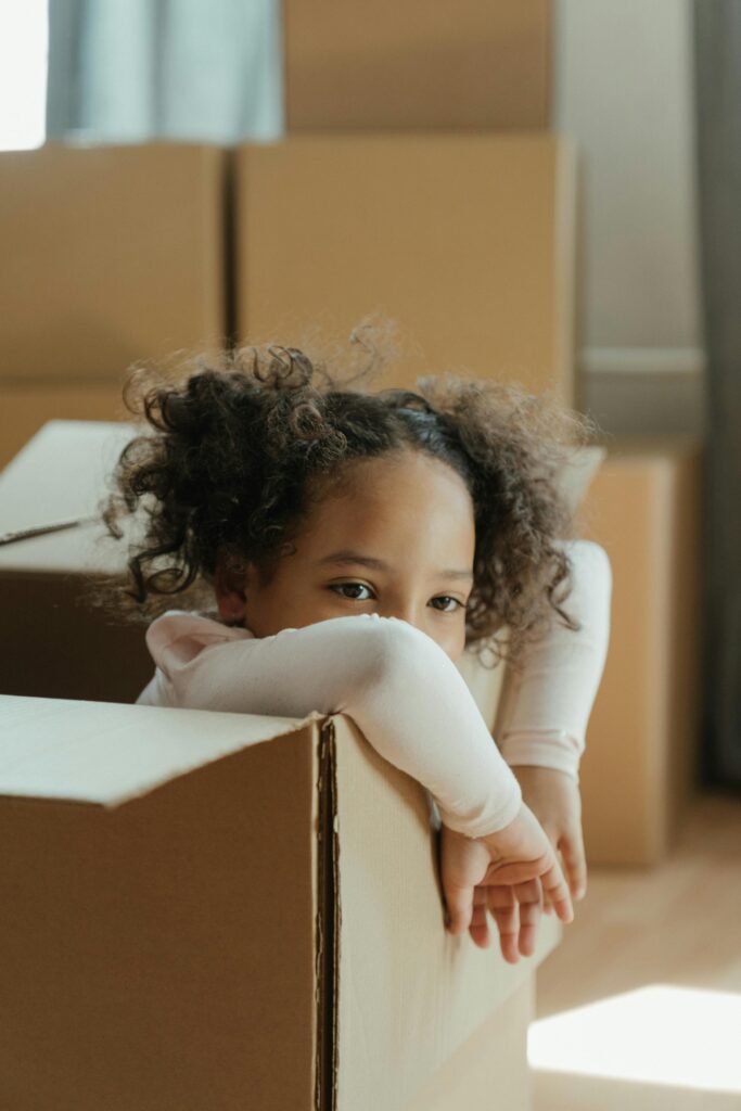 Adorable child with curly hair peeking from a cardboard box on moving day. Perfect relocation concept.